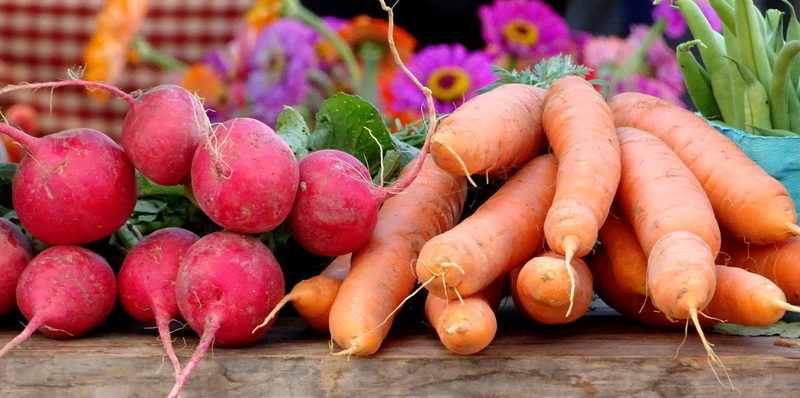 Fresh radishes and carrots with flowers at a market stand